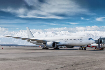 Modern white wide body passenger plane at the gateway at winter airport on the background of high snow capped mountains