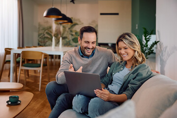 Happy couple surfing the net on laptop while relaxing in their living room.