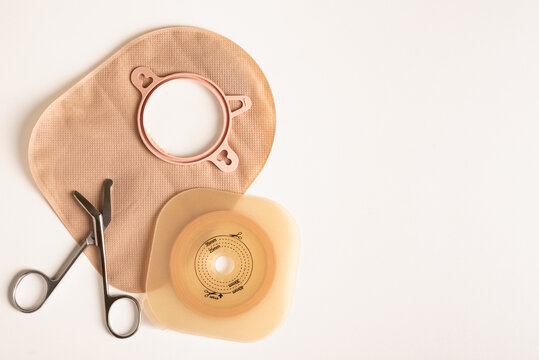 Preparing to change an ostomy bag and adhesive barrier with scissors on a white background and copy space.