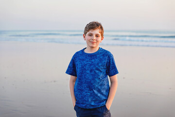 Happy cheerful teenager standing on beach at sunset. happy preteen boy smiling at the camera. Kid on family vacation at the sea.