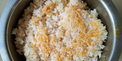 A metal bowl is filled with cooked white rice, sprinkled with what appears to be lentils or small...