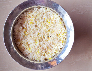 A bowl filled with fluffy white rice displays a slight yellow tint on some grains. The metallic sheen of the bowl contrasts with the neutral background.