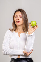 Attractive brunette young woman holding a green apple and standing on a white background. Copy space