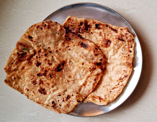 Two pieces of flatbread are placed on a round metal plate. The bread has a golden-brown color with dark spots, indicating it has been cooked well.