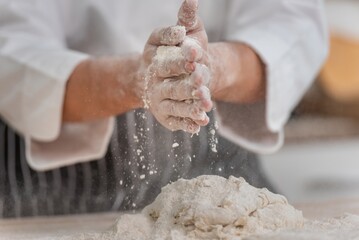 professional Chef sifting flour powder and sprinkling ingredients on massaging dough for bakery cooking. Chef show dirty finger hand sifting flour wheat and kneading dough mixing powder.