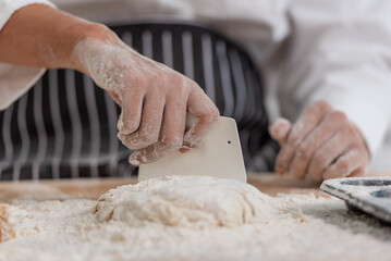 professional Chef sifting flour powder and sprinkling ingredients on massaging dough for bakery cooking. Chef show dirty finger hand sifting flour wheat and kneading dough mixing powder.