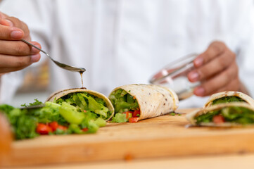chef make tortilla wrap vegetable salad slice by knife on cutting board and mix sour salad dressing in small bowl glass with wine and olive oil. tortillas wrap vegetable and juicy liquid sour dressing