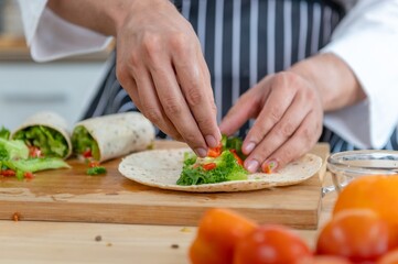 chef make tortilla wrap vegetable salad slice by knife on cutting board and mix sour salad dressing in small bowl glass with wine and olive oil. tortillas wrap vegetable and juicy liquid sour dressing