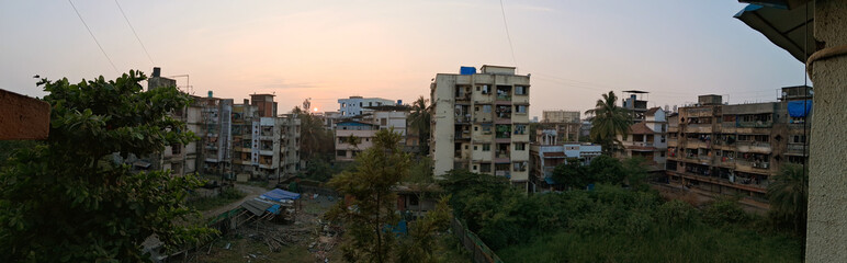 Obraz premium A panorama captures a cityscape with densely packed apartment buildings at sunset, surrounded by greenery and open spaces. 