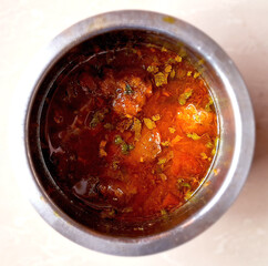 A stainless steel bowl contains a rich reddish-brown curry garnished with fresh green herbs. The dish appears to have chunks of meat or vegetables, adding texture to the flavorful liquid.