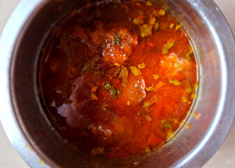 A bowl of vibrant, orange-red curry is garnished with fresh herbs, likely cilantro, and specks of seasoning. The metal container provides a stark contrast to the rich colors of the dish.
