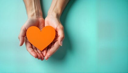 Obraz premium Hands hold orange heart against teal background. Community support, appreciation symbolised. Positive emotions, charity shown in simple gesture. Hands offer help gratitude. Kindness represented in