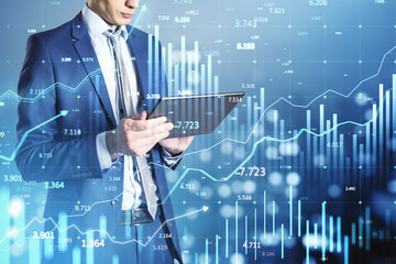 Businessman analyzing financial data on tablet with digital chart overlay in blue background. Concept of trading, stock market, and fintech.