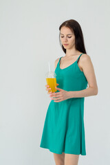 Young attractive girl in a short green dress with a cocktail in her hands on a white background