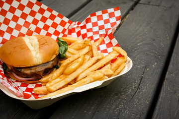 American style cheeseburger on a paper box with french fries. The background is a wooden balcony.