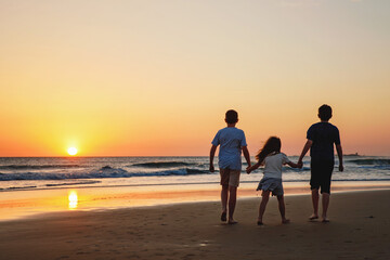 Fototapeta premium Three kids silhouettes running and jumping on beach at sunset. happy family, two school boys and one little preschool girl. Siblings having fun together. Bonding and family vacation.