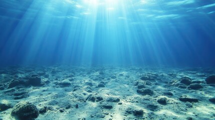 Fototapeta premium Underwater scene with sunlight rays penetrating the water's surface, illuminating the ocean floor covered with rocks and sand.