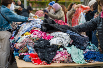 People looking at a pile of second hand clothes in a flea market.