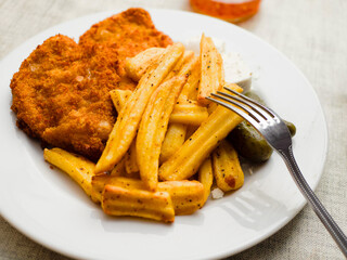 Breaded chicken fillet meal and fried potatoes chips with ridges on a white plate and light color table cloth. Simple food made of high quality premium products. Cooked poultry meat.