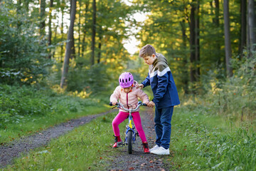 Cute little preschool girl in safety helmet riding bicycle. School kid boy, brother teaching happy...