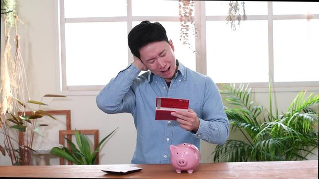 銀行通帳を見ながら困る若いアジア人男性