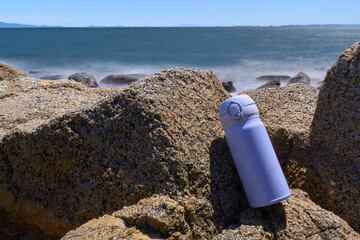 海岸の岩場に置かれた水色の水筒
