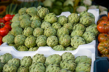 a bunch of green artichoke are stacked on white plastic containers.
