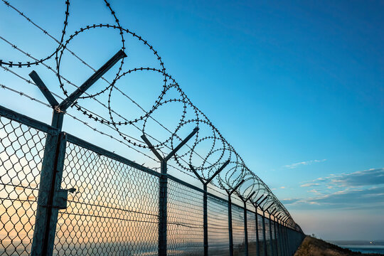 Fence With Barbed Wire in Front of a Great Blue Sky - Concept of Freedom, Liberty, or Confinement
