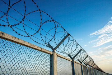 Fototapeta premium Fence With Barbed Wire in Front of a Great Blue Sky - Concept of Freedom, Liberty, or Confinement
