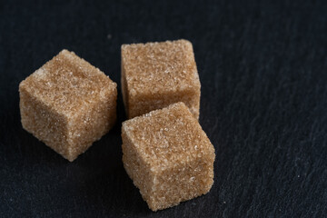 Brown cane sugar cubes on dark stone background, closeup.