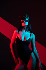 Seductive Woman in a Cat Mask Holding a Whip Explores BDSM Themes in a Vibrant, Modern Setting at Night