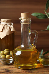 Bottles of fresh olive oil and olives with leaves on wooden background