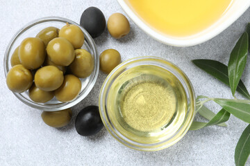Bowl of fresh olive oil and olives with leaves on light background