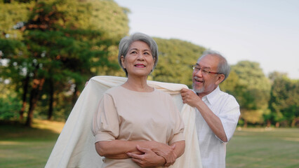 Asian senior couple wears or cover a blanket in the public garden, Elderly retirement family taking care of each other and outdoor concept