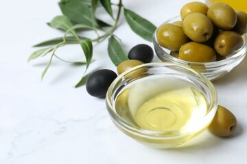 Bowl of fresh olive oil and olives with leaves on white background