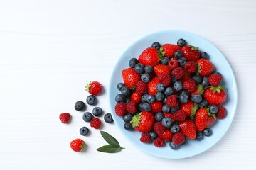 Different fresh ripe berries in bowl on wooden table, top view