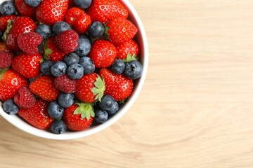 Different fresh ripe berries in bowl on wooden table, top view