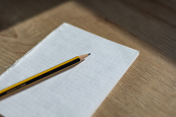 Pencil lies on a used checkered notepad on a wooden desk. Office utensils; business; workplace; office stuff.