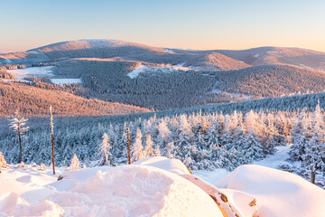 Eastern Sudetes, View of snowy mountain range from hiking trail during winter hike in the mountains, viewpoint of wide winter landscape in the mountains at sunset.