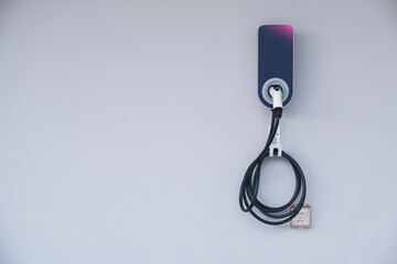 Modern electric vehicle (Ev) charging station with power cable plug for charging Ev or hybrid car, isolated on white house wall.