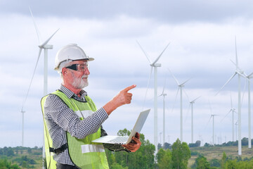 An engineer sits at his laptop looking at a clean energy wind turbine project to generate electricity.