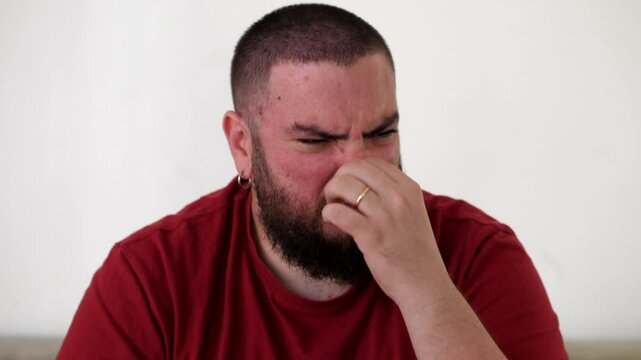 Reacting to a bad smell, the young man covers his nose and waves his hands in an attempt to rid himself of the unpleasant odor.