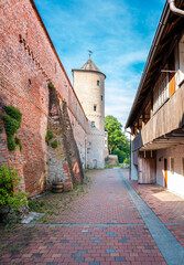 A picturesque view of a historic brick wall in Donauworth, Germany, with round tower. Cobblestone path leads towards the tower.