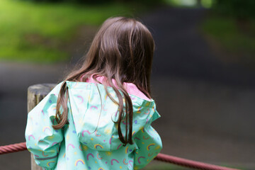 Lonely sad girl on the playground in a raincoat. Concept of difficult childhood and psychological...