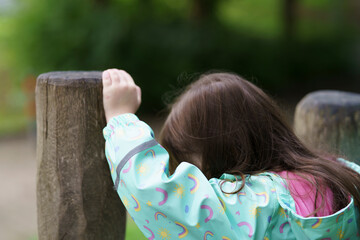 Lonely sad girl on the playground in a raincoat. Concept of difficult childhood and psychological...