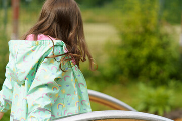 Lonely sad girl on the playground in a raincoat. Concept of difficult childhood and psychological...
