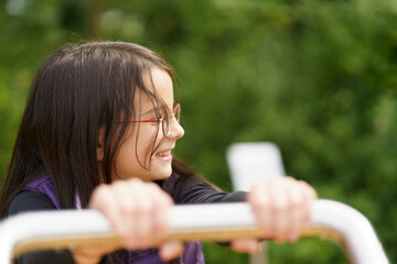 A little cute smiling girl in glasses and a purple vest plays on the playground. Happy childhood...