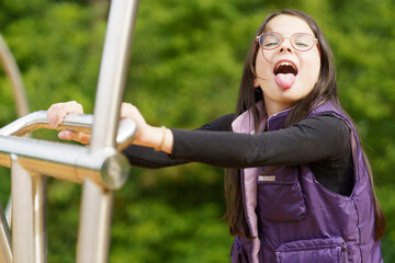 A little cute smiling girl in glasses and a purple vest plays on the playground. Happy childhood...