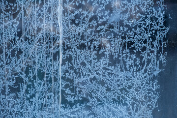 Glass frost pattern. A beautiful frosty pattern on the dark glass of the house. Full frame. Abstract winter. The concept of frost, cold, and frost. Beautiful surface for winter postcard design