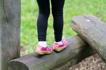 Close-up photo of little children's feet in sneakers walking on a log on a playground. Happy childhood concept